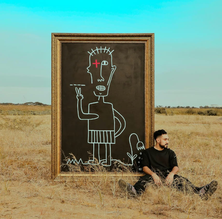 Esteban Jácome sentado junto a una de sus pinturas de gran formato, enmarcada, en un descampado